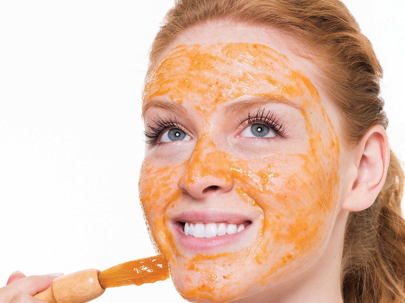 Meisje met een borstel zet een masker van wortelen op haar gezicht