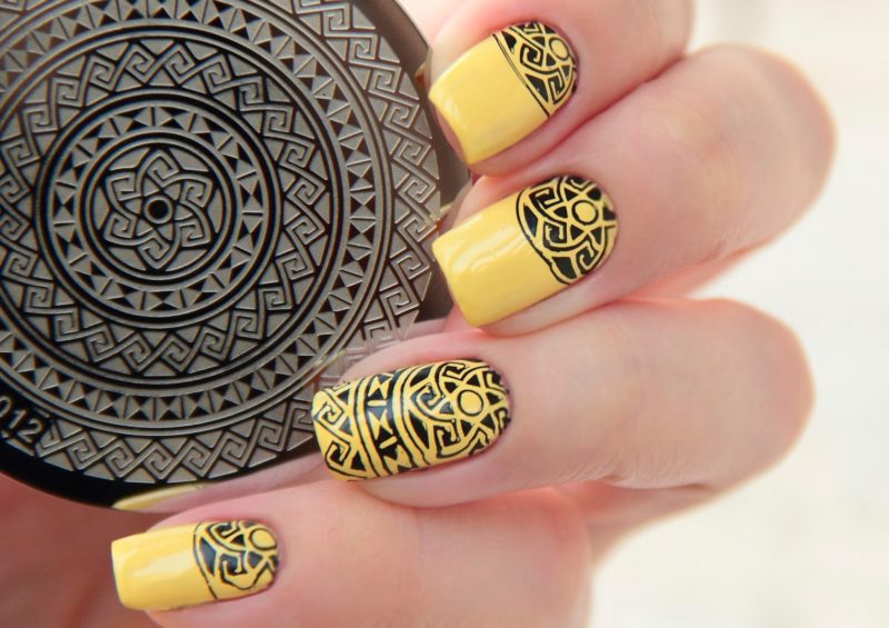 Żółty manicure z czarnym wzorem etnicznych znaczków.