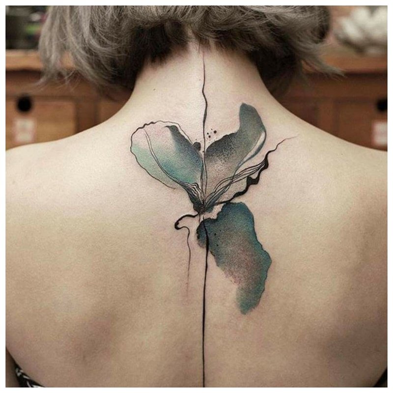 Tatouage aquarelle en forme de fleur entre les omoplates